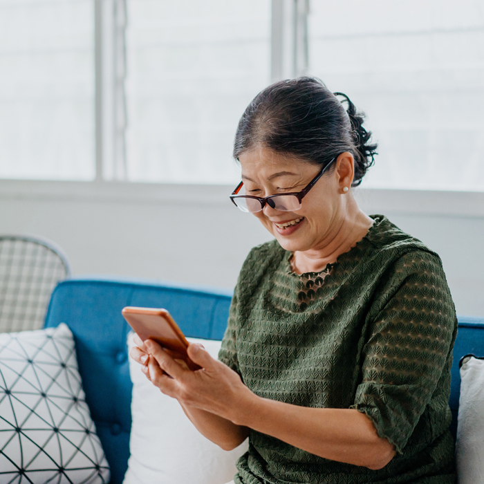 A smiling Patelco member on their couch using the easy-to-use Patelco Mobile App